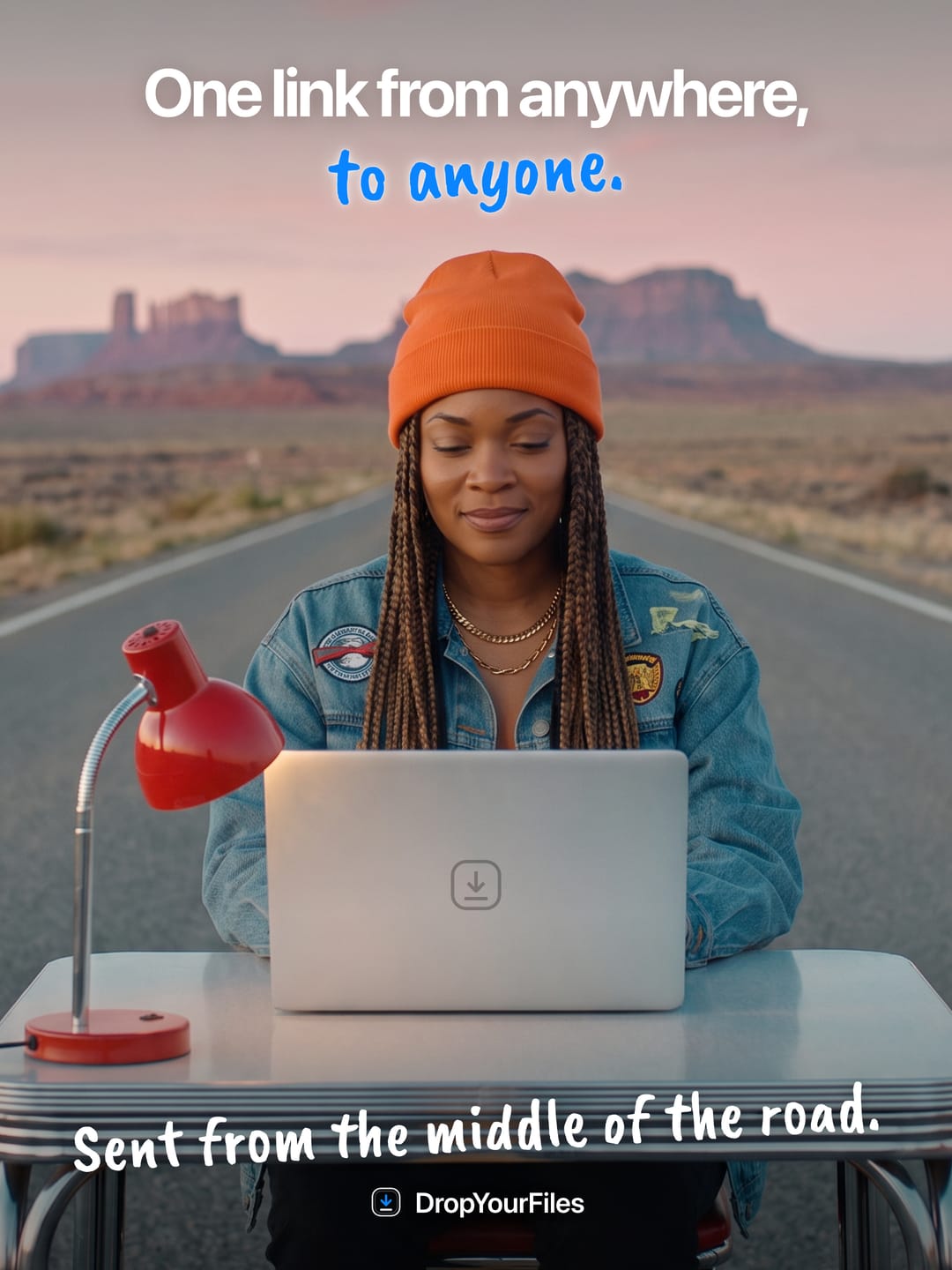 A woman in an orange beanie at a laptop on a desk in the middle of a desert road. The headline reads “One link from anywhere, to anyone.” and the line at the foot, “Sent from the middle of the road.”