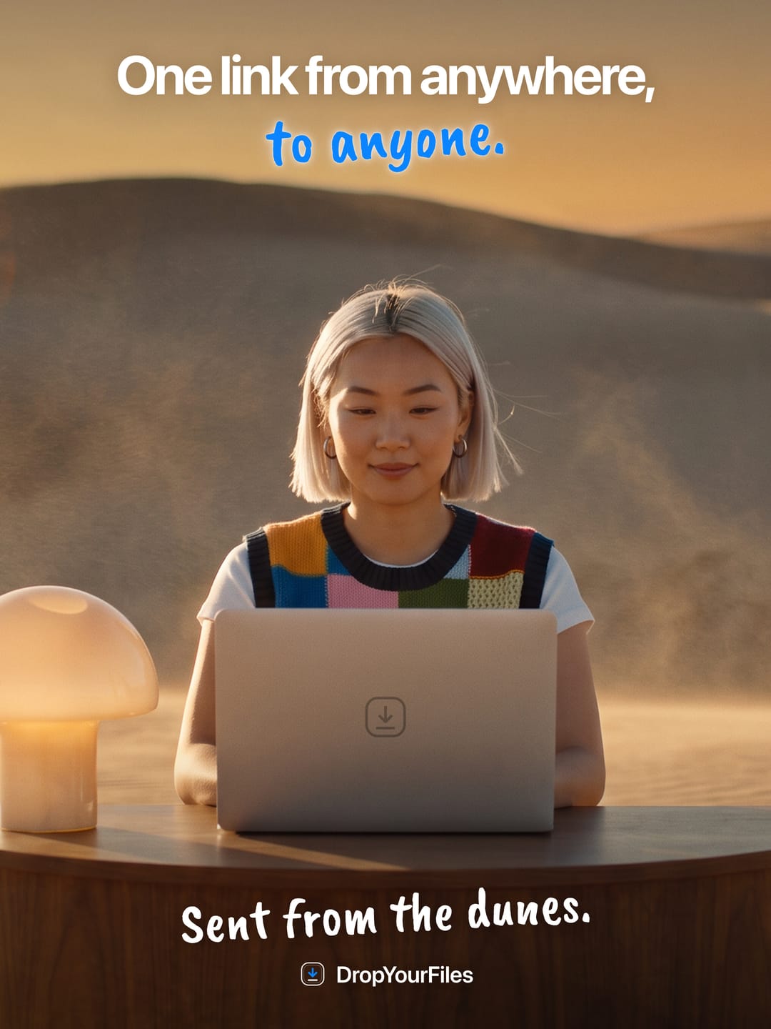 A woman at a laptop on a desk in the sand dunes at golden hour. The headline reads “One link from anywhere, to anyone.” and the line at the foot, “Sent from the dunes.”